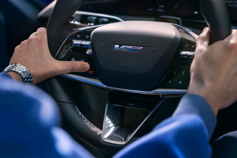Close-up of a Man About to Press the V-Button on the 2026 OPTIQ-V Steering Wheel | Faulkner Cadillac Bethlehem in Bethlehem PA